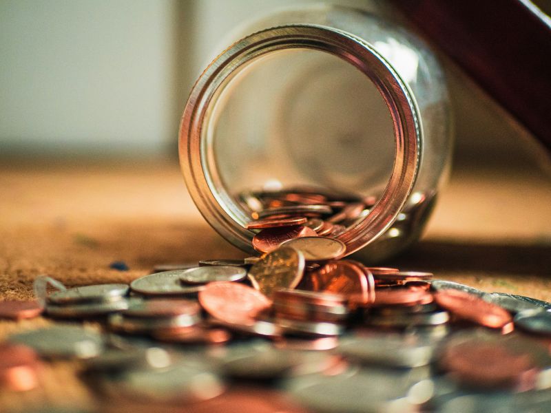 money in form of coins out of a glass jar laying on the ground